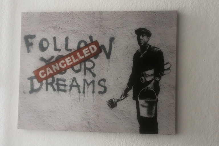 Banksy Gemälde mit Mann Pinsel, Eimer und Plakate haltend neben schwarzen Graffiti „Follow your Dreams“ mit roten Stempel „Cancelled“ darauf neben ihm