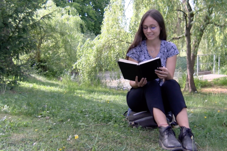 Studentin sitzt lesend im Park
